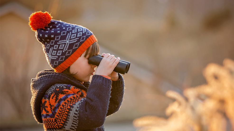 Cute little child, boy, exploring nature with binoculars, looking at sunset